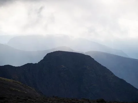 Mountain peaks in the clouds. A chain of gray mountains in the backlight Stock Photos