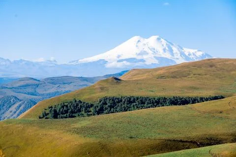 A mountain range and Mount Elbrus with a snow covered peak and a green valley Stock Photos