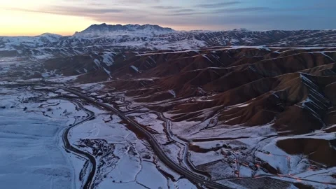 A mountain range covered in snow and a rocky desert at sunset time Stock Footage 328246830