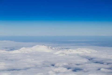 Mountain range emerging from endless white clouds, aerial shot. Stock Photos