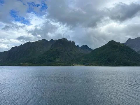 Mountain range with lake under cloudy sky in nature scene Stock Photos