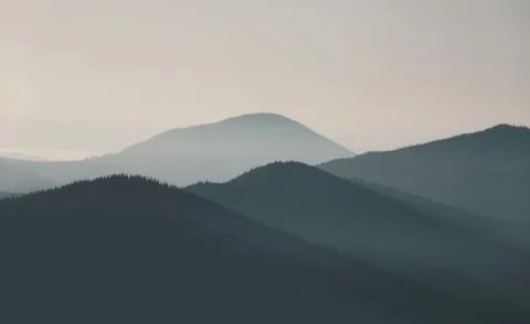 Mountain range landscape in soft blue tones with morning fog at sunrise. Stock Photos