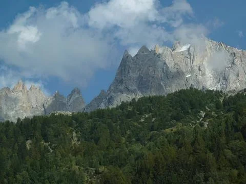 Mountain range with rocky peaks and green forest below Stock Photos