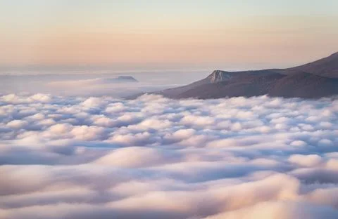 A mountain range sticking out from under colorful clouds drenched by the sun  Stock Photos