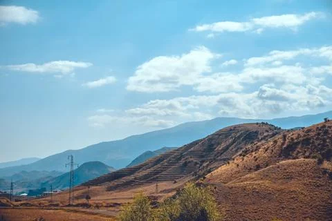 A mountain range stretches under a blue sky, with trees in view Stock Photos