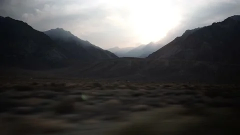Mountain Range with Sunset Peaking Through Clouds, Driving View Stock Footage 146563015