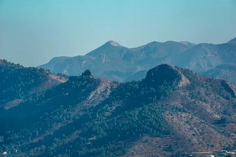 A mountain range with trees on its slopes under a blue sky Stock Photos