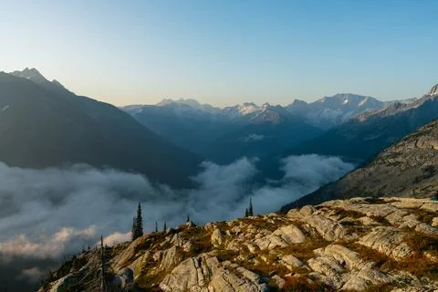 Mountain range view with clouds hanging low in the valley and rocky foregroun Stock Photos