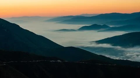 Mountain range with visible silhouettes through the morning colorful fog Stock Photos