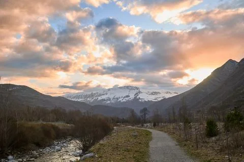 Mountain river and trekking path against the backdrop of snow-capped mountain Stock Photos