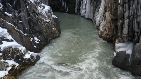 A mountain river between steep cliffs covered in ice, aerial footage in 4k Stock Footage 106064764