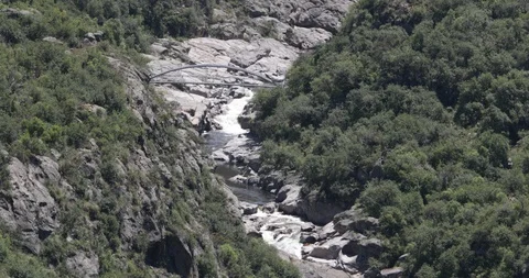 Mountain river with falls in eroded rocky basin with woods and pedestrian bridge 스톡 동영상 118999536