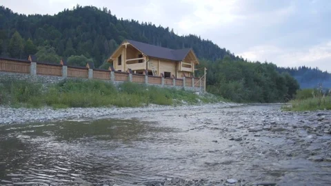 A mountain river flows along the forest and a lovely wooden house Stock Footage 79728719