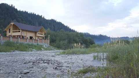 A mountain river flows along the forest and a lovely wooden house Stock Footage 79728787