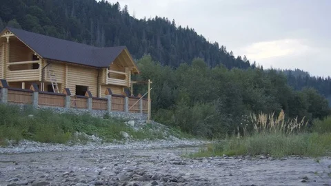 A mountain river flows along the forest and a lovely wooden house Stock Footage 79728911