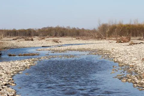 A mountain river flows along a stone beach on a sunny day Stock Photos