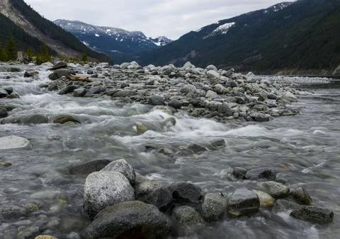 Mountain river flows over smooth stones in a serene valley surrounded by peak Stock Photos