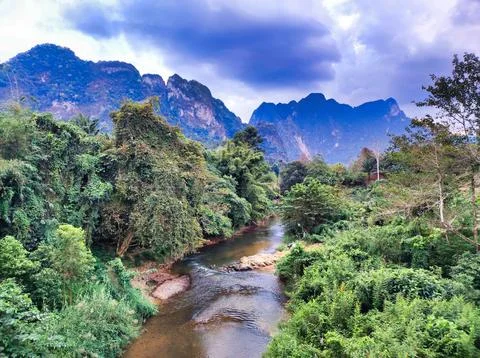 Mountain river flows through green forest under cloudy sky in remote area. .. Stock Photos