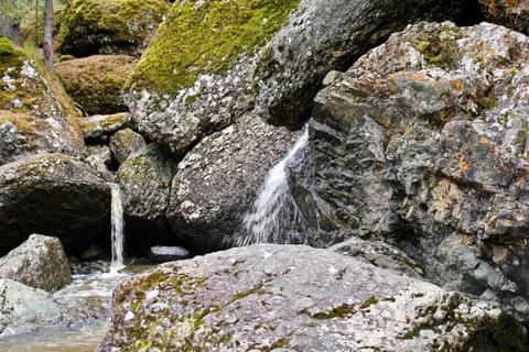A mountain river waterfall flows through a river bed through huge boulders with Stockfoto's
