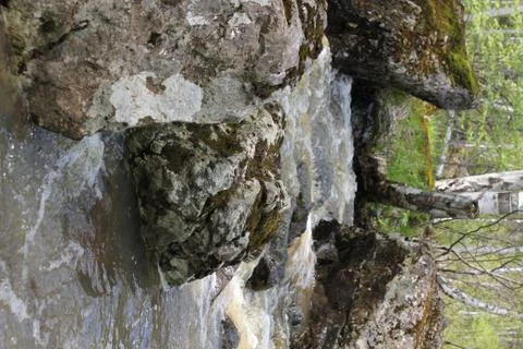 A mountain river waterfall flows through a river bed through huge boulders with Stock-Fotos