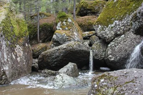 A mountain river waterfall flows through a river bed through huge boulders with 写真素材