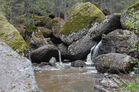 A mountain river waterfall flows through a river bed through huge boulders with 写真素材