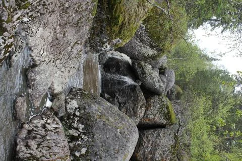 A mountain river waterfall flows through a river bed through huge boulders with 写真素材