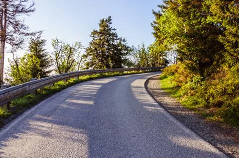 Mountain road between the trees with a blue sky on the background Stock Photos