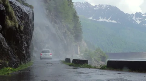 On mountain road car passes under a waterfall hitting the road Stock Footage 50966032