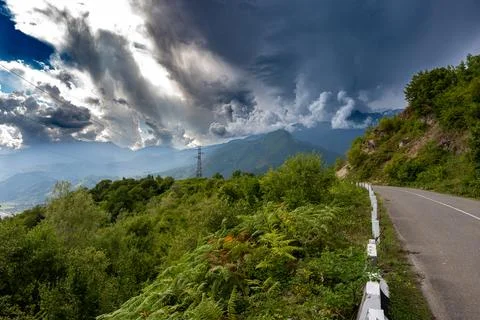 Mountain road with grass and trees just before thunderstorm Stock Photos