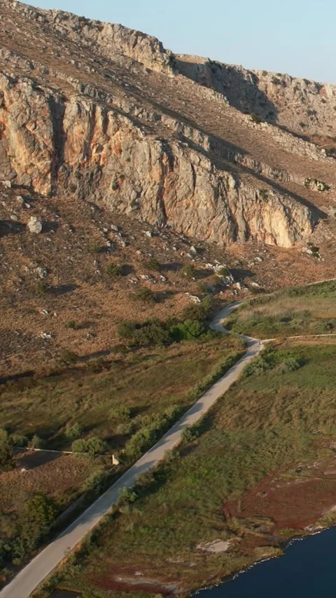 Mountain Road Passing Beneath Massive Rock Cliff Above Valley Vídeo Stock 344108047