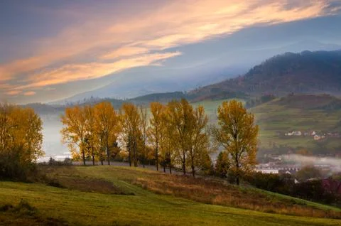 Mountain road with trees along a path with a mountain village in sunrise autu Stock Photos