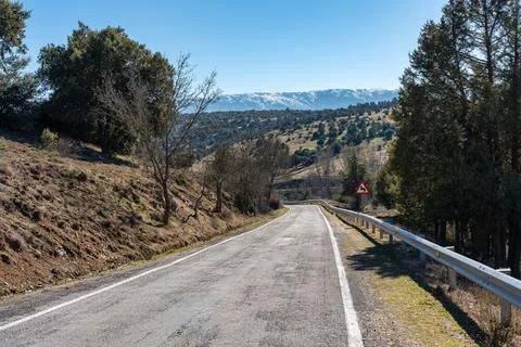 Mountain road that winds through the forest towards the snowy mountains next to Stock-Fotos