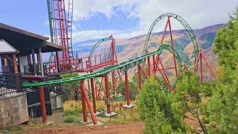 Mountain roller coaster speeds through green loops and steep turns above Stock Footage 346030681