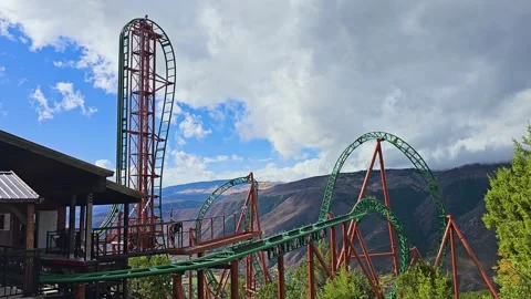 Mountain roller coaster twists through loops and towering drops, with green Stock Footage 345250143