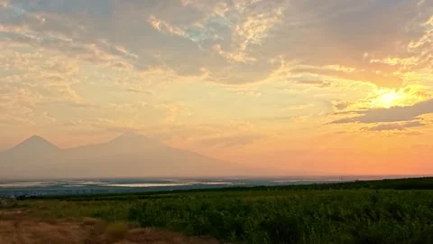 Mountain silhouette at sunset, glowing sky, green fields below Stock Footage 339641327