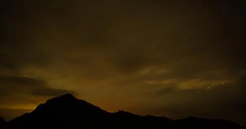 Mountain silhouetted by a night sky of clouds illuminated by artificial light. Stock Photos