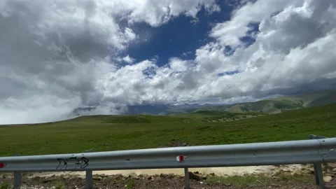 Mountain slopes. Blue sky, white clouds above the ground, green grass. Road 02 Stock Footage 155619790