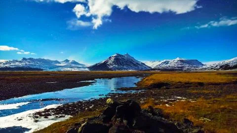 Mountain stream, around which is an empty field and mountains Stock Photos