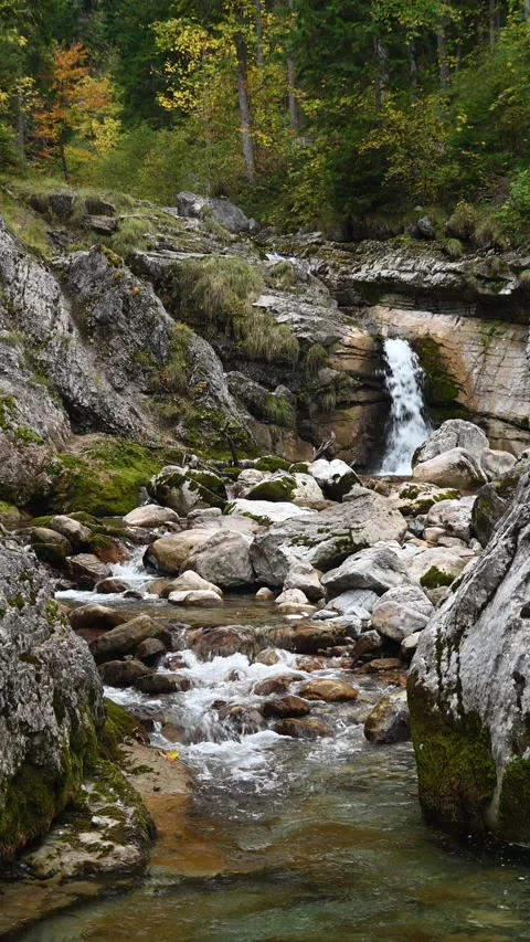 A mountain stream between rocks and a waterfall in the background in autumn Stock-Footage 260871812
