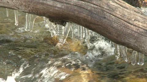 Mountain stream flowing beneath log with icicles- tight shot Stockbeeldmateriaal 52914316