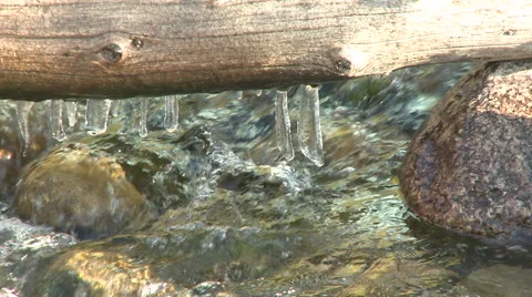 Mountain stream flowing beneath log with icicles tight right Stock Footage