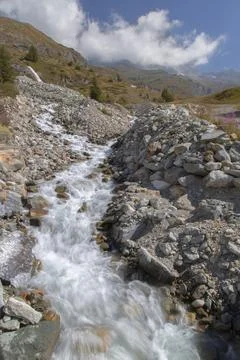Mountain stream flowing over rocks in sunny alpine landscape Stock Photos