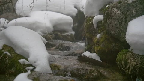 Mountain stream flowing through snow covered rocks Vidéo 331793078