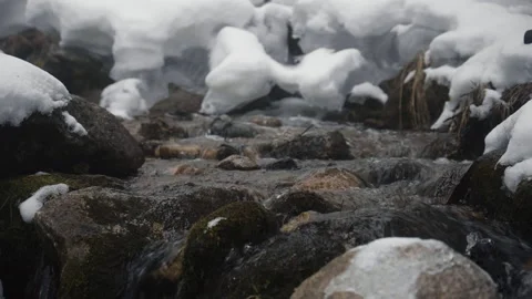 Mountain stream flowing through snow covered rocks Vidéo 331798014