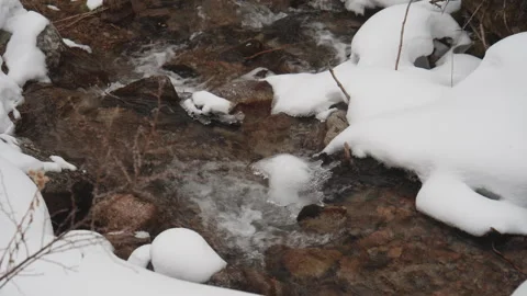 Mountain stream flowing through snow covered rocks Stock Footage 331798653
