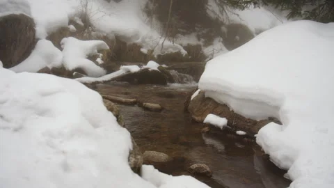 Mountain stream flowing through snow covered banks Stock Footage 331800761