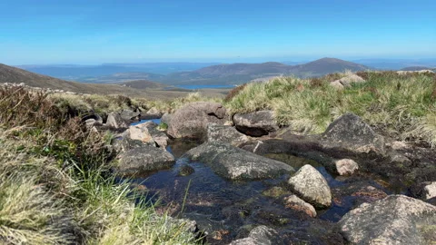 Mountain stream flowing towards valley on sunny day with blue sky Stock Footage 319571725