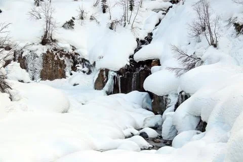 Mountain stream flows among the rocks and puffy white snow on the banks Stock Photos