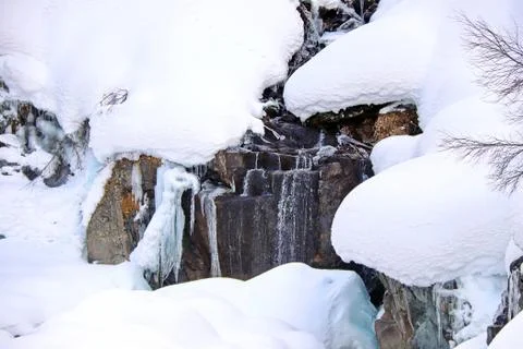 Mountain stream flows among the rocks and puffy white snow on the banks Stock Photos